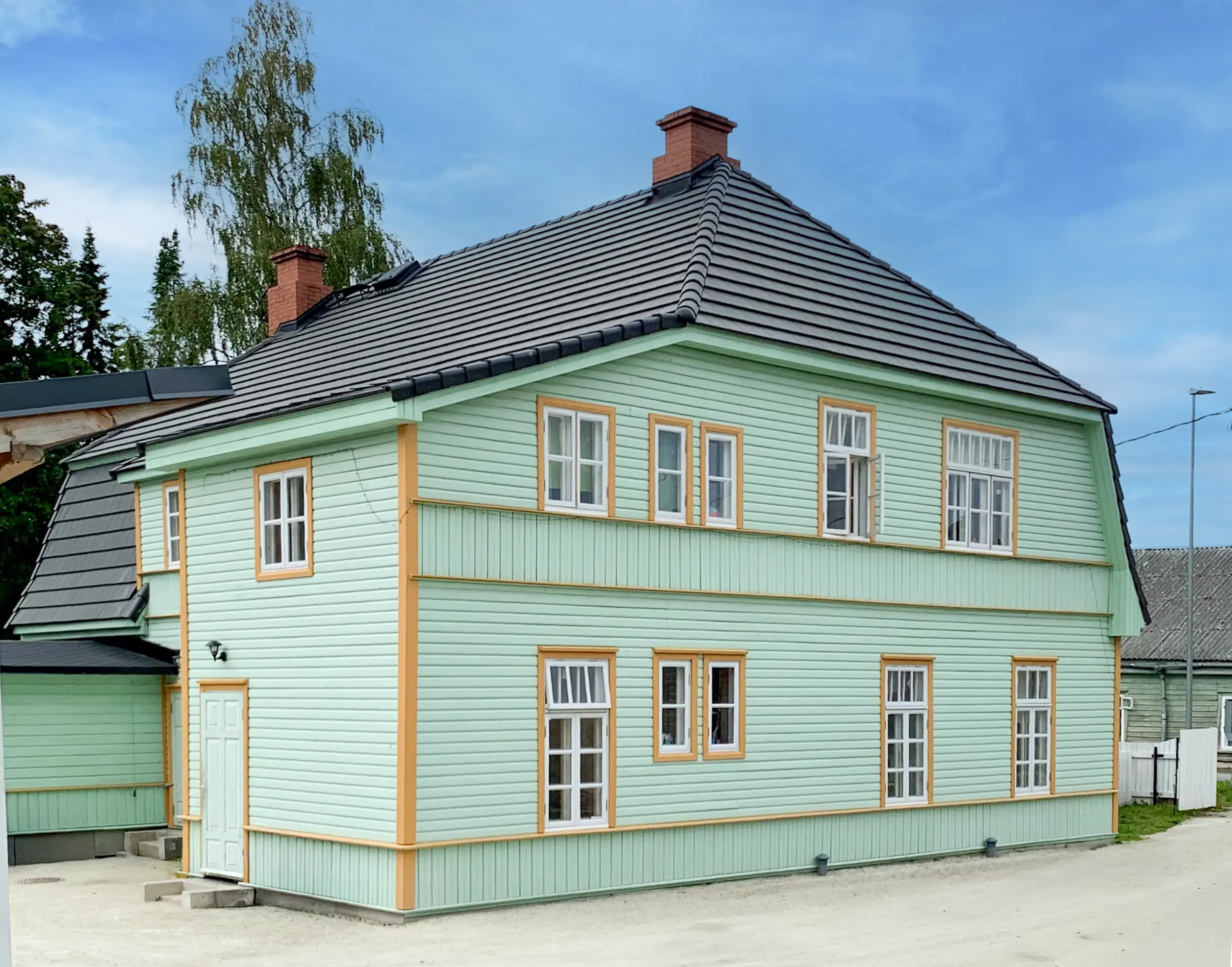 Jugendstilvilla in Paide Estland mit hellgrünem Holz und gelben Zierelementen in einer Seitenansicht.